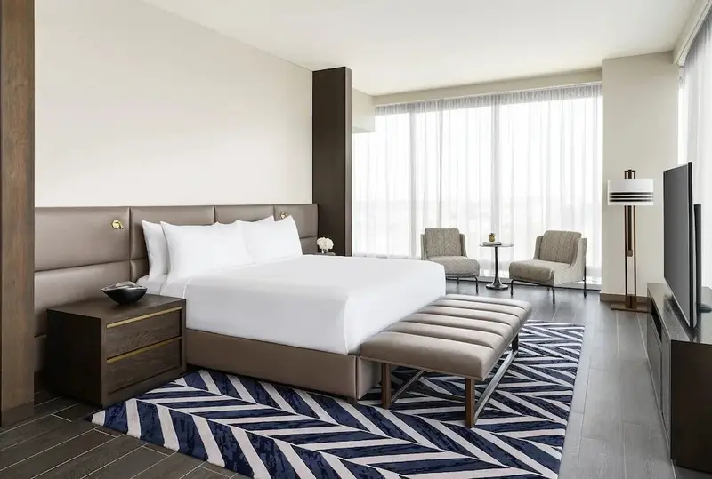 Une chambre lumineuse avec un grand lit et deux fauteuils près d'une fenêtre.