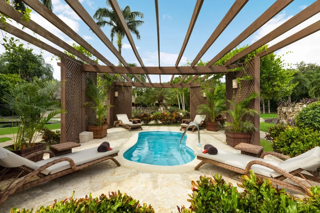 Espace de détente extérieur avec petite piscine et chaises longues ombragées par une pergola.