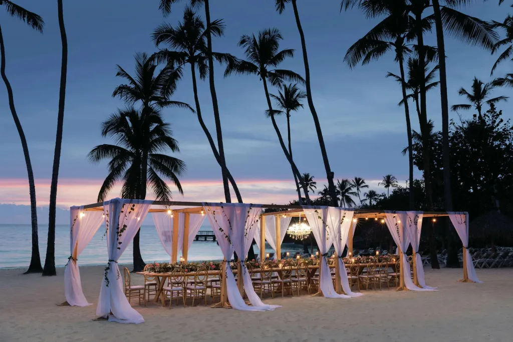 Une table de fête est dressée sur une plage de sable fin au coucher du soleil.