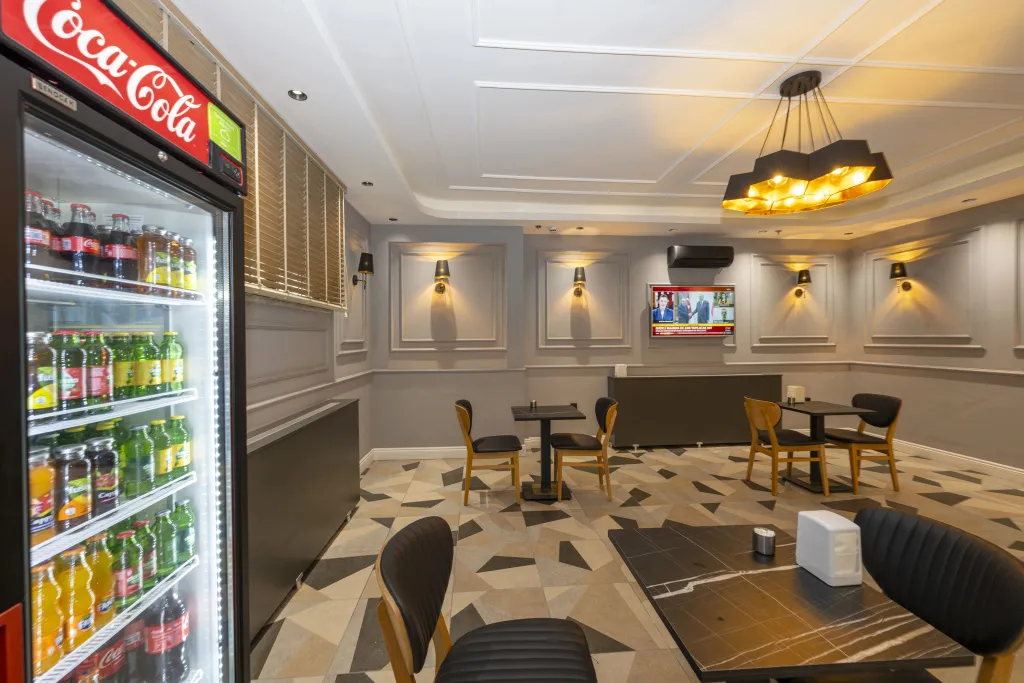 Une salle lumineuse avec des tables et des chaises dispose d'un réfrigérateur rempli de boissons.
