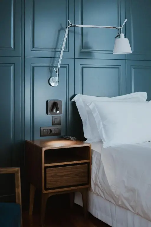 Une table de chevet en bois est placée à côté d'un lit recouvert de draps blancs.