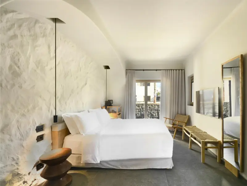 Une chambre lumineuse avec un grand lit recouvert de draps blancs et un mur en pierre texturée.