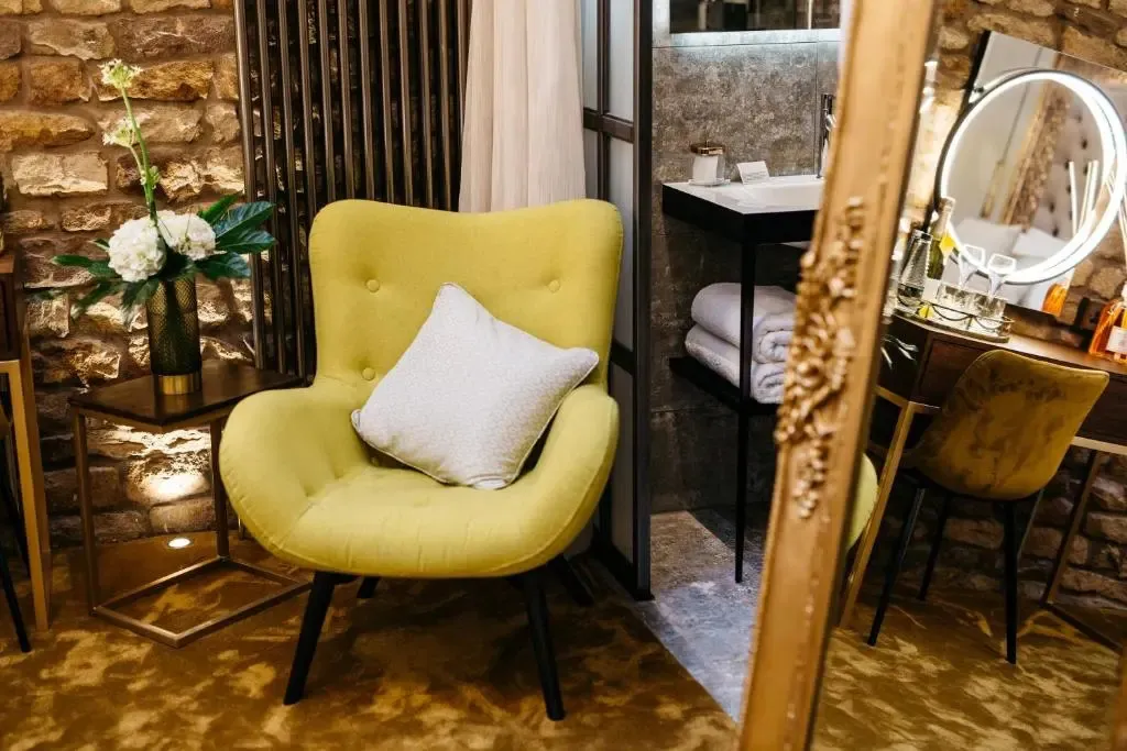 Un fauteuil jaune et un coussin clair se trouvent dans un intérieur décoré de pierres apparentes.