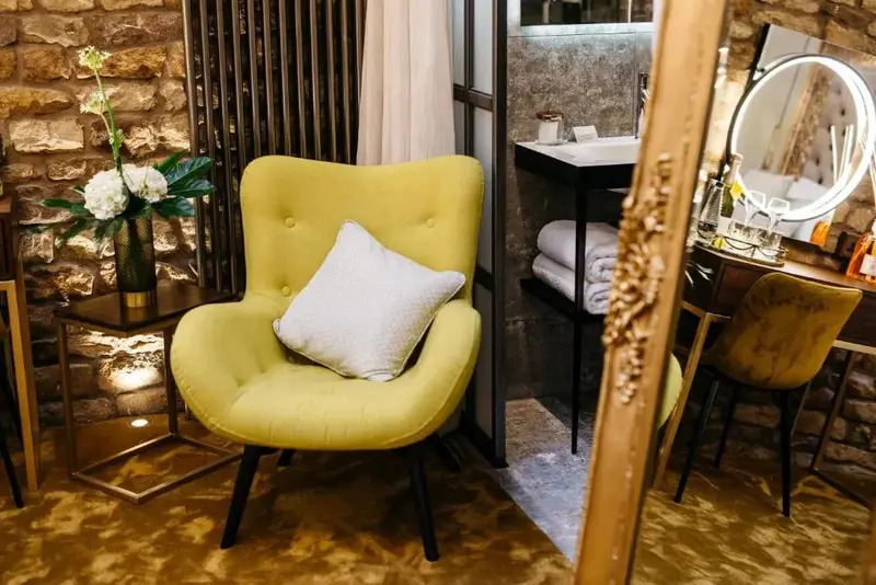Un fauteuil jaune et un coussin clair se trouvent dans un intérieur décoré de pierres apparentes.