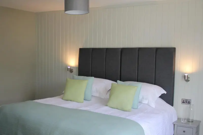 Une chambre lumineuse avec un grand lit recouvert d'une couette turquoise et de coussins verts.