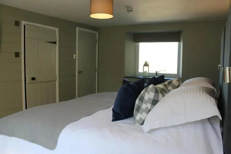 Une chambre lumineuse avec un grand lit recouvert de linge blanc et des oreillers bleus.