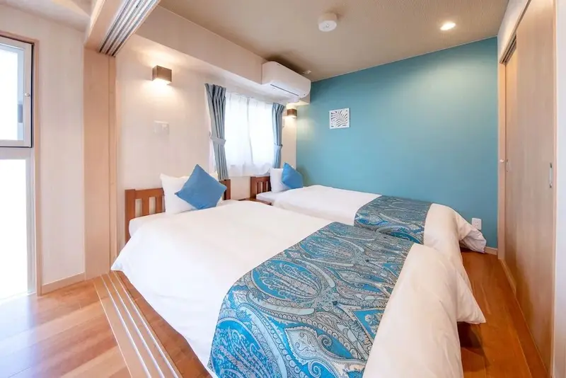 Une chambre lumineuse avec deux lits simples et un mur bleu turquoise.
