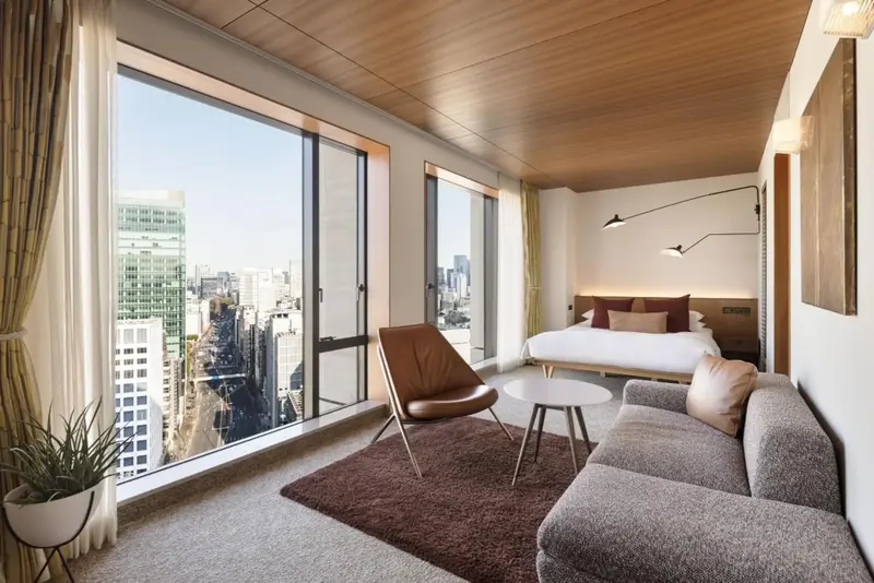Une chambre lumineuse avec un grand lit et un coin salon donnant sur une vue urbaine.