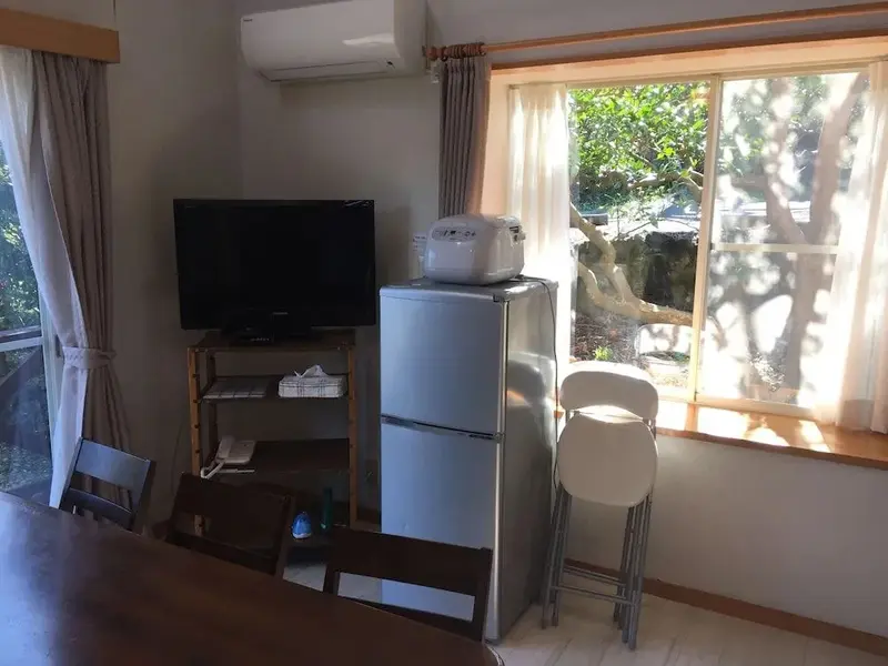 Une pièce lumineuse avec un réfrigérateur, une télévision et une table.