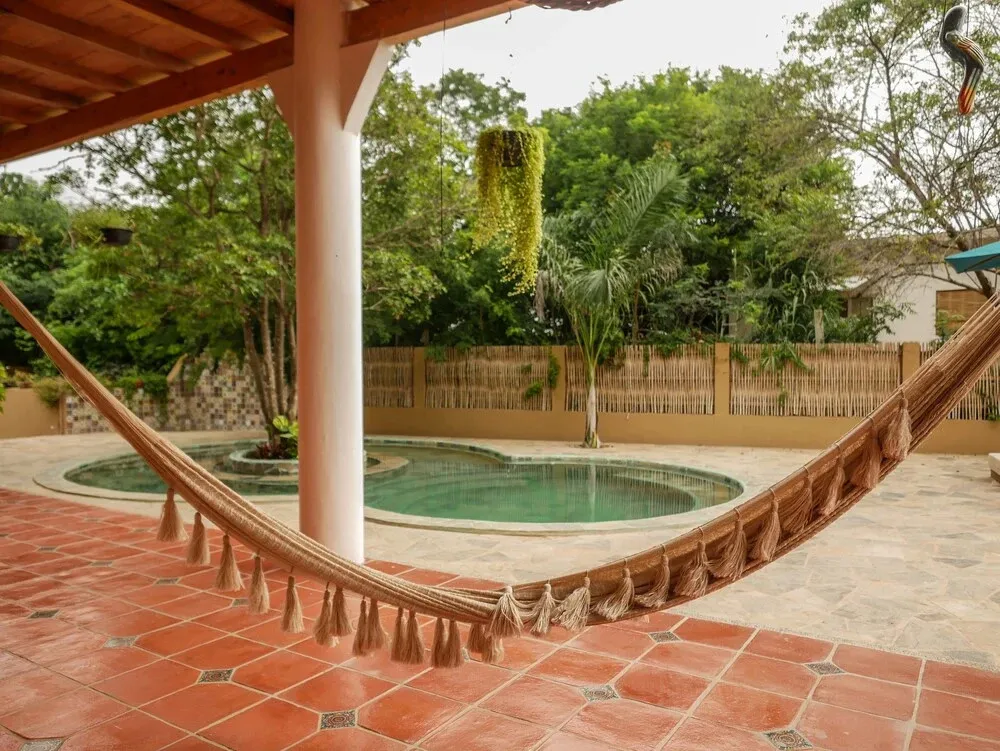 Un hamac est suspendu au-dessus d'une terrasse carrelée près d'une piscine.