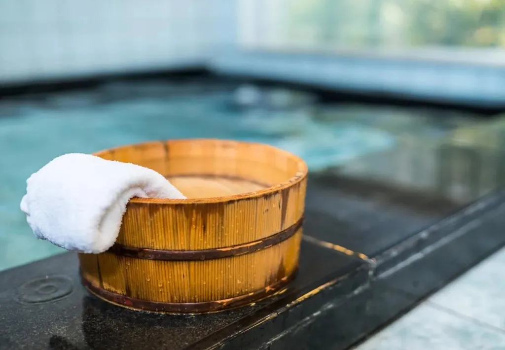 Un seau en bois avec une serviette blanche près d'une piscine intérieure.