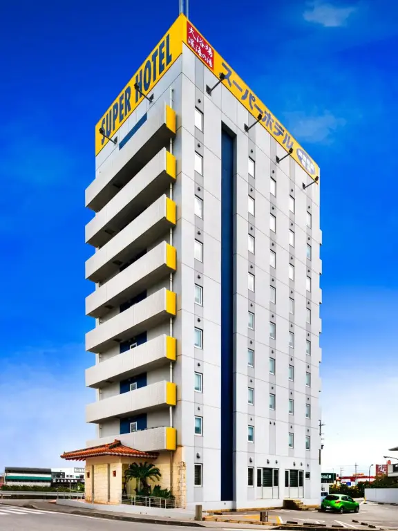 Bâtiment moderne à plusieurs étages avec des balcons et une façade blanche et jaune sous un ciel bleu.