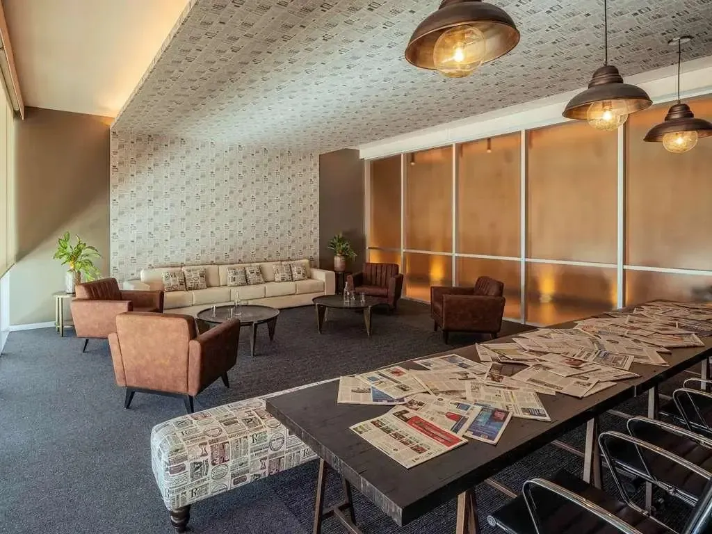 Un espace de détente intérieur avec canapés, fauteuils et une longue table recouverte de journaux.