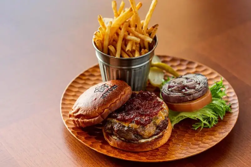 Un hamburger coupé en deux est servi avec des frites et des légumes sur une assiette en métal.