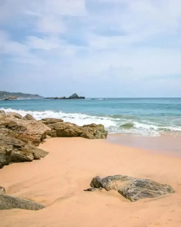 Une plage de sable fin bordée de rochers et de vagues turquoise.