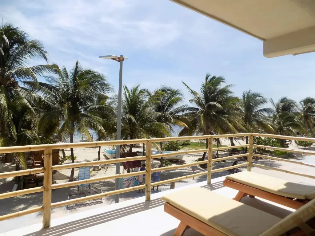 Terrasse avec transats donnant sur une plage de sable blanc bordée de palmiers.
