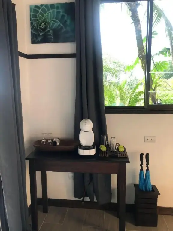Une machine à café et des verres sont posés sur une commode en bois près d'une fenêtre.