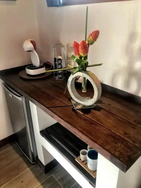 Un plan de travail en bois sombre présente une machine à café et une composition florale.