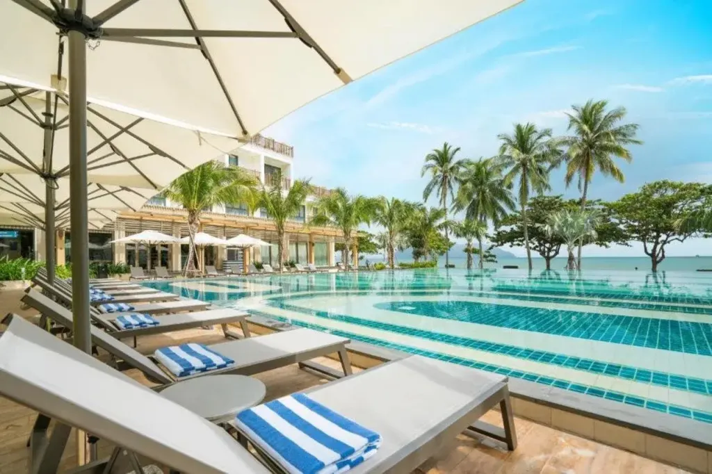 Transats blancs alignés au bord d'une piscine turquoise avec vue sur la mer.