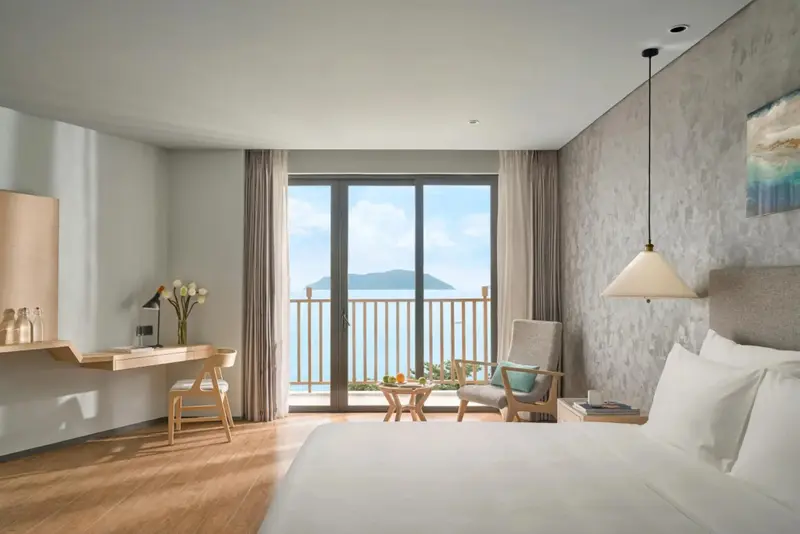 Une chambre lumineuse avec un lit fait et un accès à un balcon offrant une vue sur la mer.