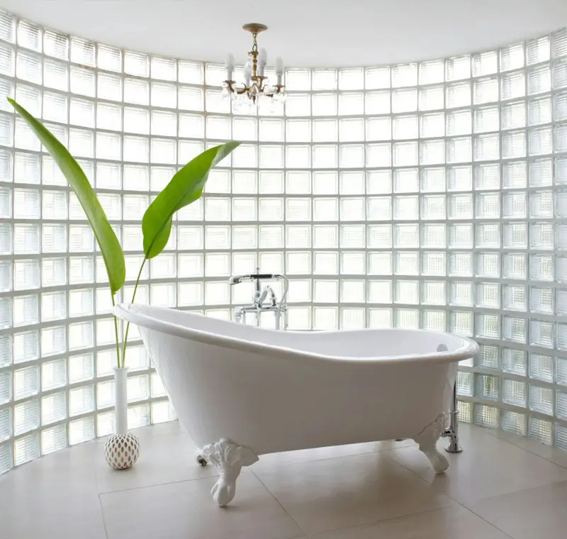 Une baignoire sur pieds se trouve dans une salle de bain lumineuse avec un mur en briques de verre.