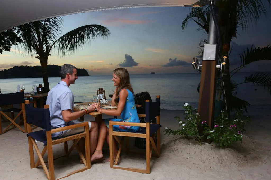 Un couple dîne à une table en bois sur une plage au coucher du soleil.