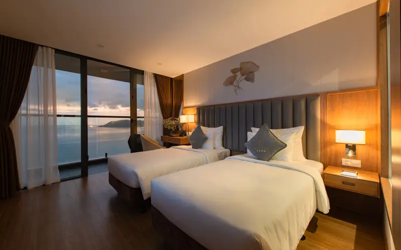 Chambre lumineuse avec deux lits simples donnant sur une vue mer.