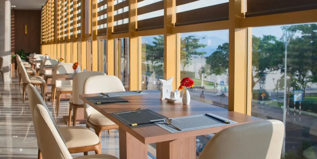Une salle lumineuse avec des tables dressées et de grandes baies vitrées donnant sur un paysage verdoyant.