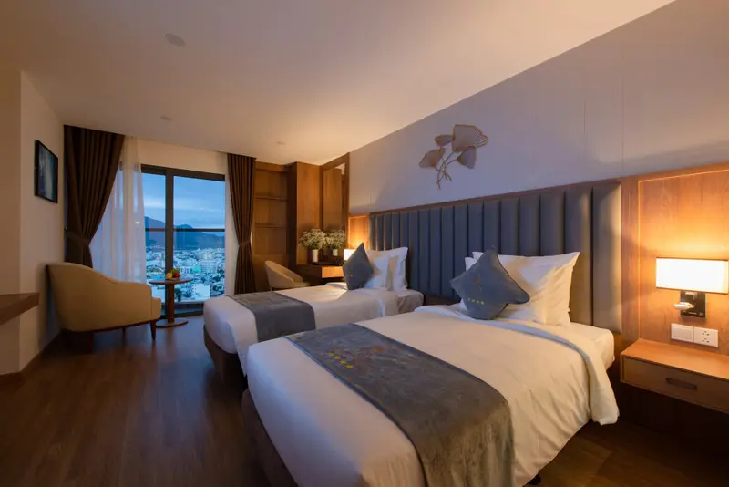 Chambre lumineuse avec deux lits simples et vue sur la ville.