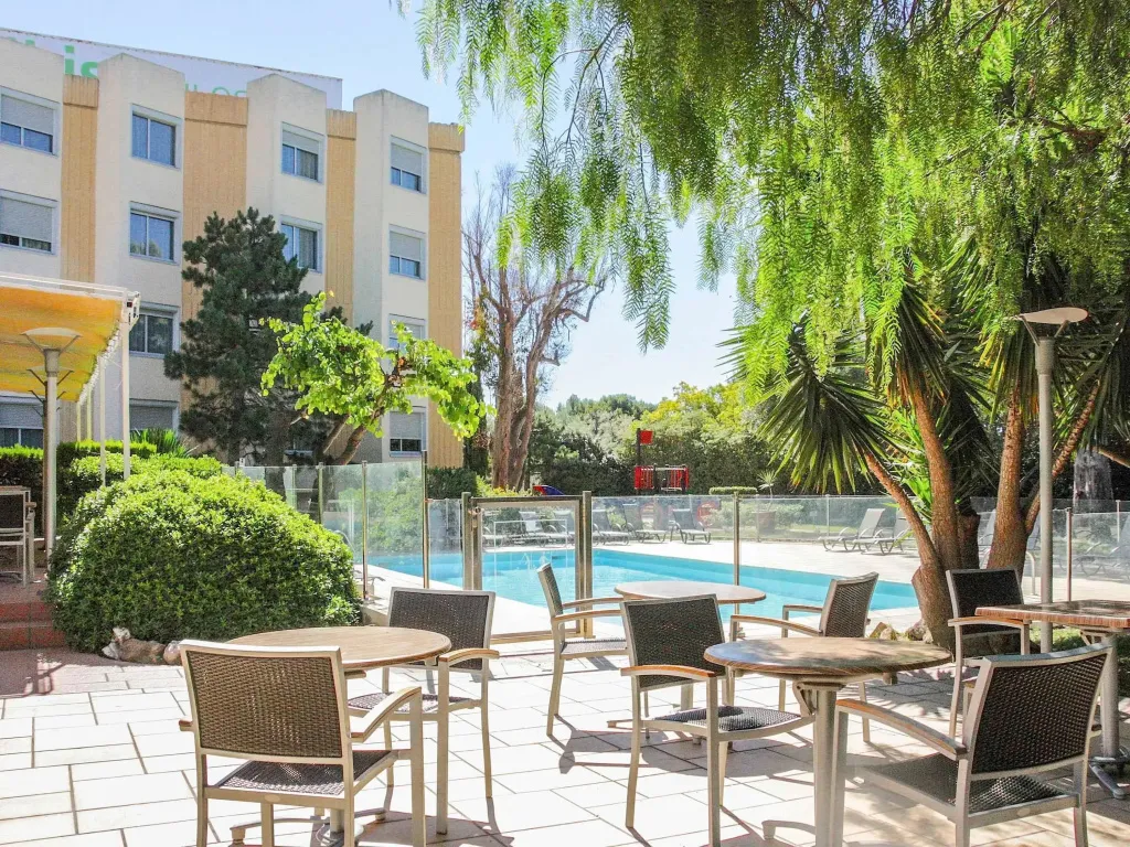 Terrasse avec tables et chaises devant une piscine et un bâtiment.