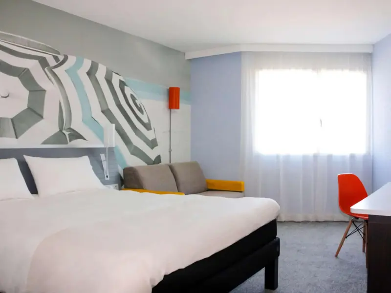 Une chambre lumineuse avec un grand lit et une décoration murale graphique.