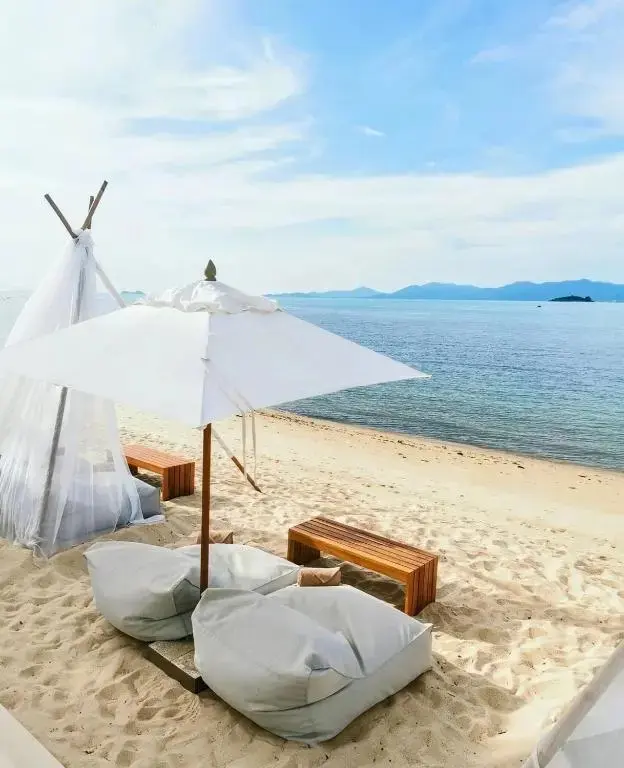 Aménagements de plage avec des coussins et des bancs en bois face à la mer.
