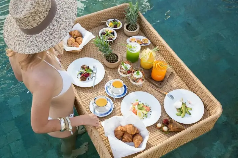 Une table basse en osier présente un assortiment de plats et de boissons au bord d'une piscine.