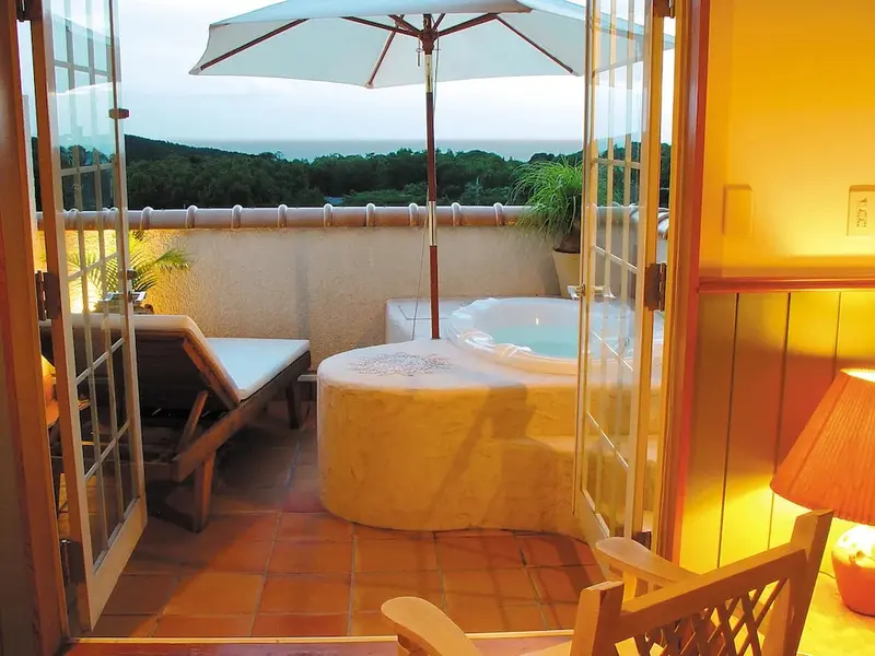 Une terrasse avec un jacuzzi et un transat offre une vue sur la végétation et la mer.