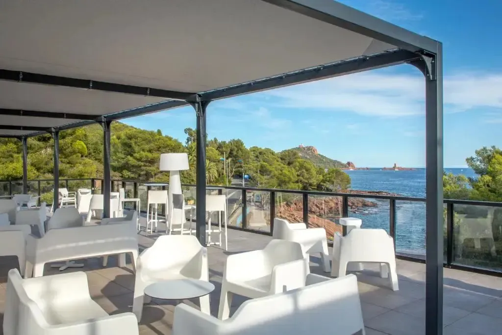 Terrasse ombragée avec mobilier blanc donnant sur la mer et une côte rocheuse.