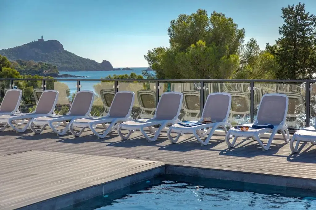Transats blancs alignés sur une terrasse en bois au bord d'une piscine, avec vue sur la mer et les collines verdoyantes.