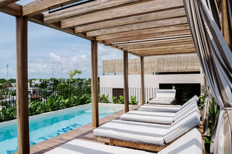Transats blancs alignés au bord d'une piscine à débordement sous une pergola en bois.