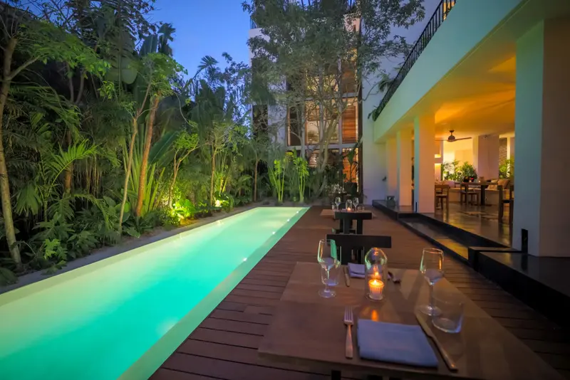 Une piscine rectangulaire bordée d'une terrasse avec des tables éclairées à la bougie.