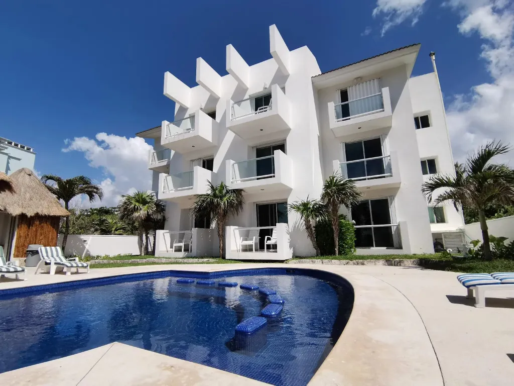 Bâtiment blanc moderne avec piscine et végétation tropicale sous un ciel bleu.