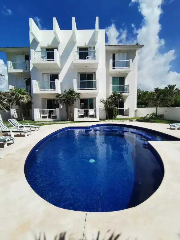 Une piscine bleue au premier plan, avec un bâtiment blanc à plusieurs étages en arrière-plan.