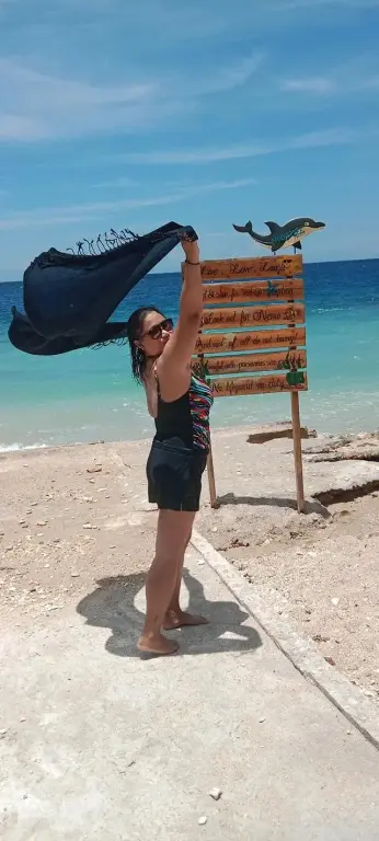 Une personne lève les bras sur une plage de sable fin face à la mer.