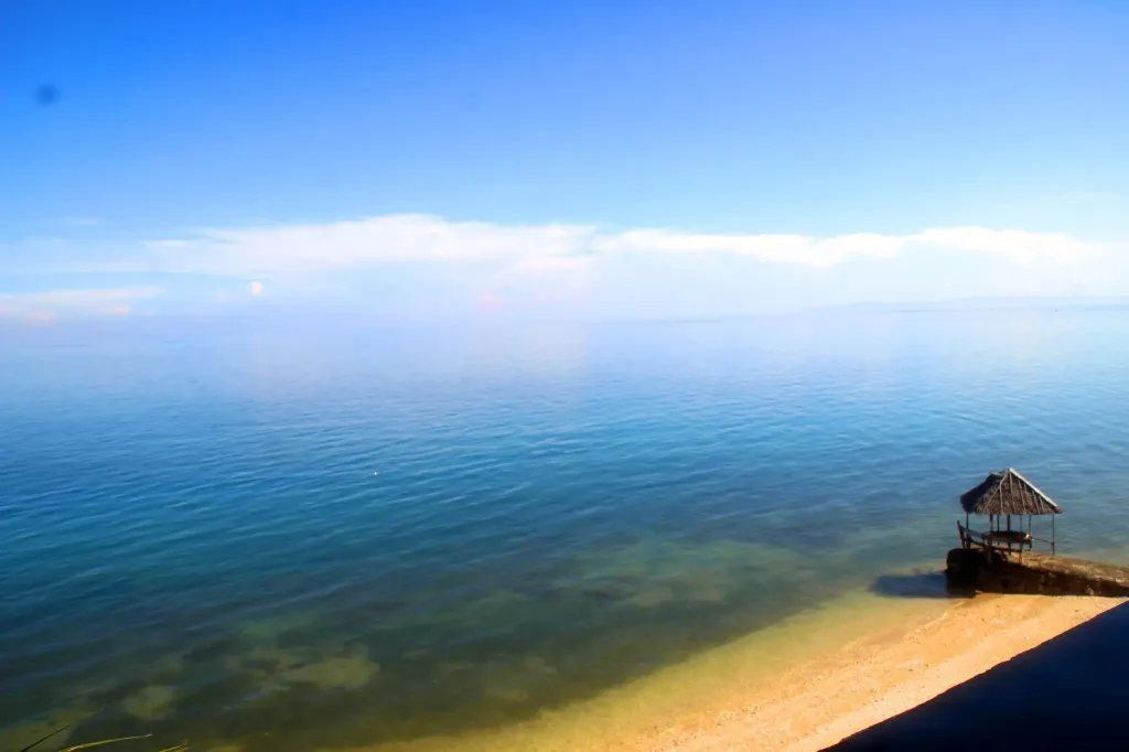 Vue sur une mer bleue et une petite structure en bois sur une plage de sable.