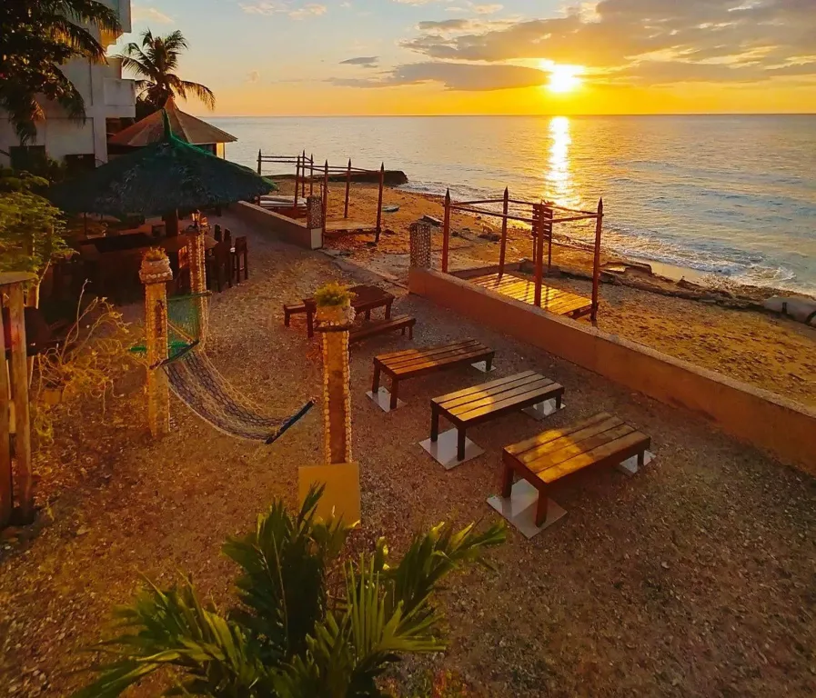 Tables et chaises en bois sur une plage de galets au coucher du soleil.