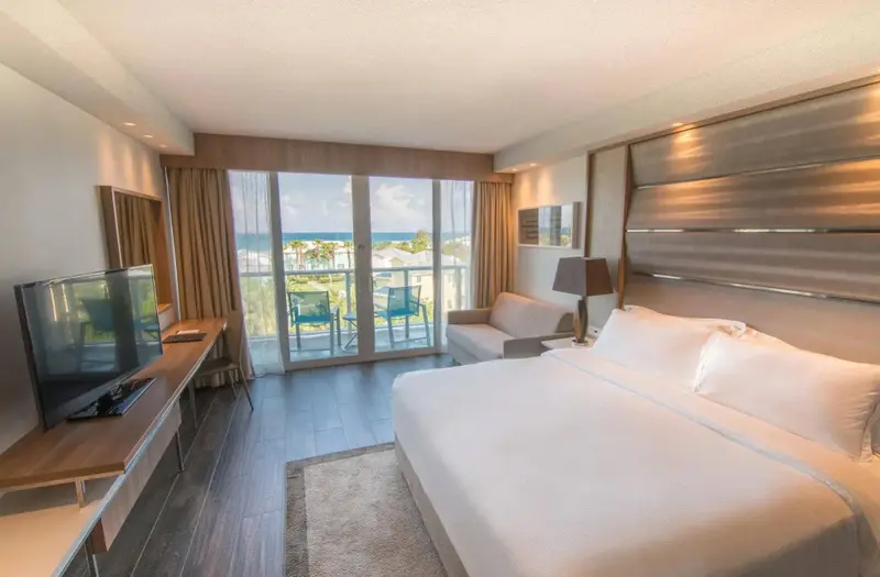 Une chambre lumineuse avec un grand lit et un accès à un balcon avec vue sur la mer.
