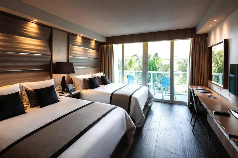 Une chambre moderne avec deux lits et un balcon donnant sur la végétation.