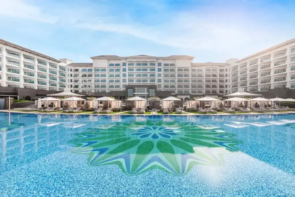 Vue d'un grand complexe hôtelier blanc avec une piscine ornée d'un motif floral.