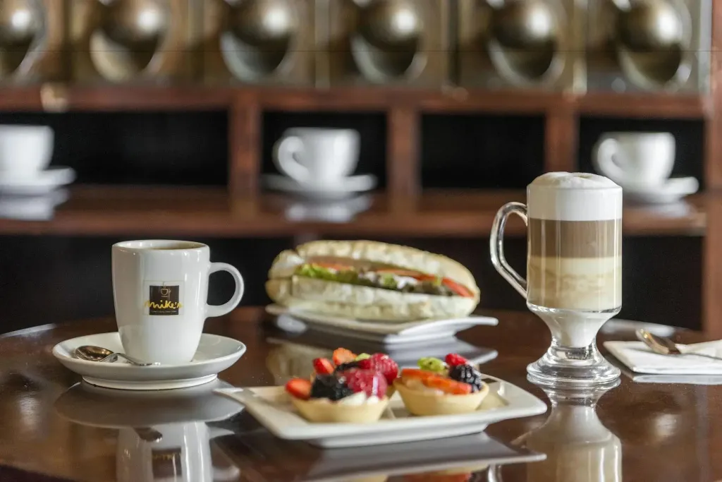 Une table présente une tasse de café, un sandwich, un verre de boisson et des tartes aux fruits.