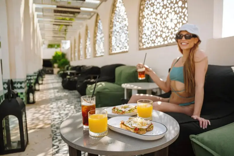 Une table servie de boissons et de toasts se trouve devant un espace de détente ombragé.