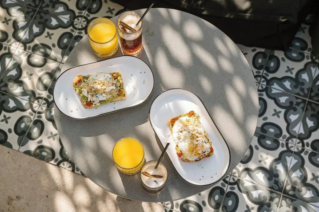 Une table ronde présente deux toasts garnis et deux verres de boissons.